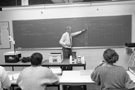 Foto van een prof die les geeft aan studenten.